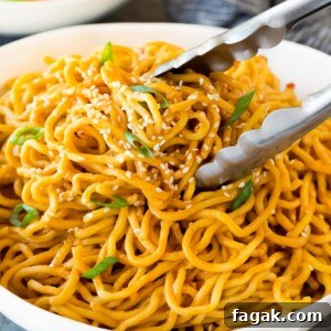 Tongs serving up a portion of sesame noodles.