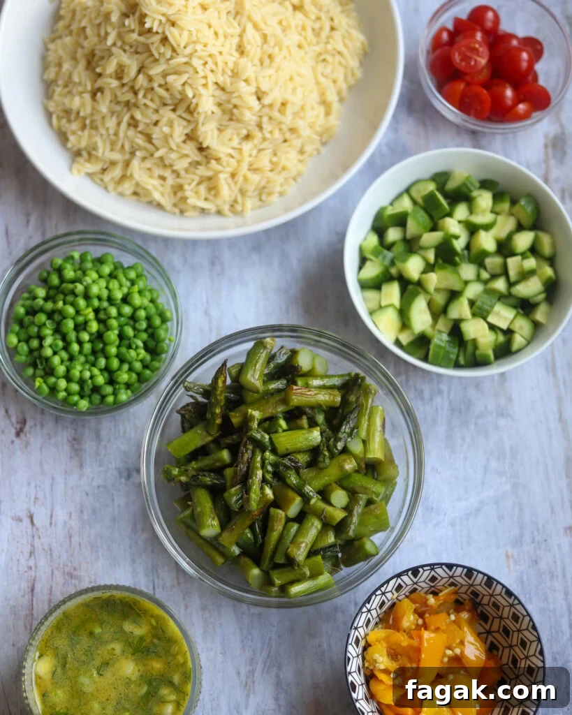 Overhead view of ingredients for asparagus orzo salad including: orzo pasta, grilled asparagus, chopped cucumber, peas, yellow grilled peppers and Dijon salad dressing in small bowls.