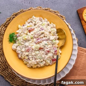 chicken salad with grapes in a yellow bowl with salad spoon and napkin on a flat surface.