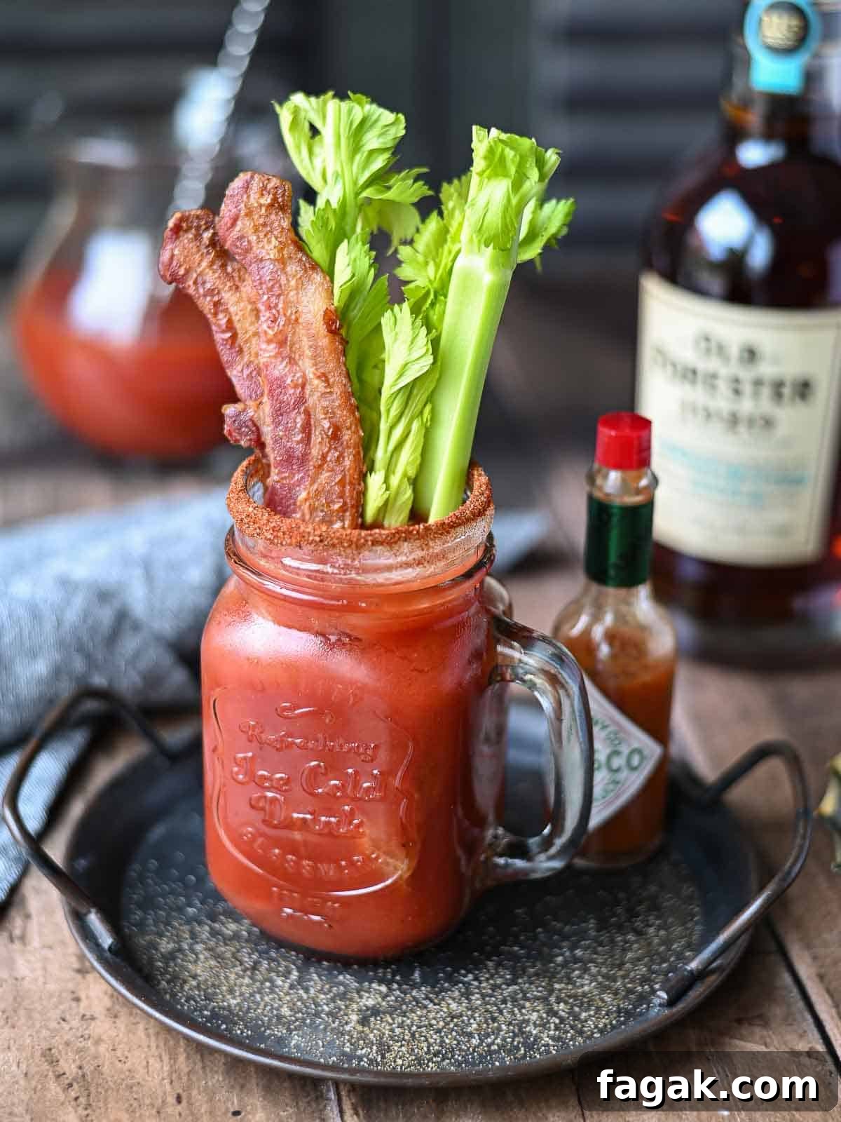 Angled view of a bacon bloody mary in a clear Mason jar on a metal tray.