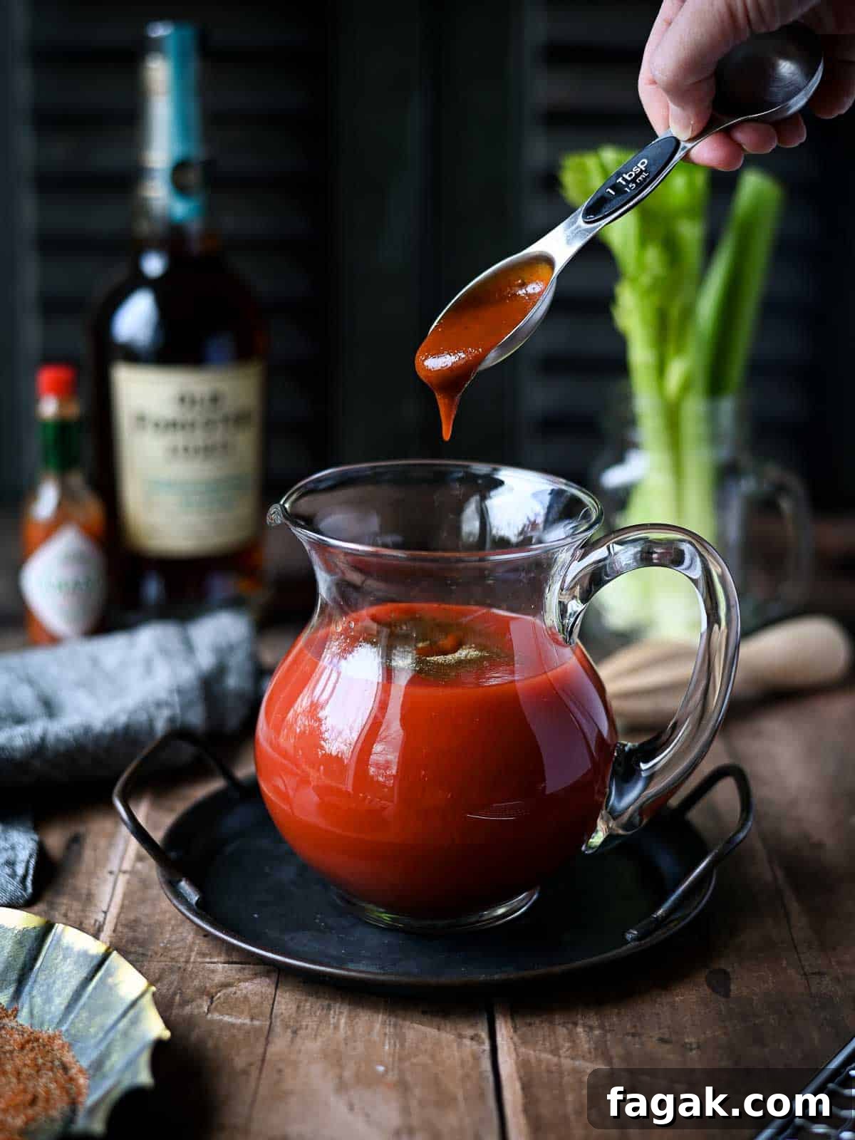 A hand adding barbeque sauce to a pitcher of bloody mary mix.
