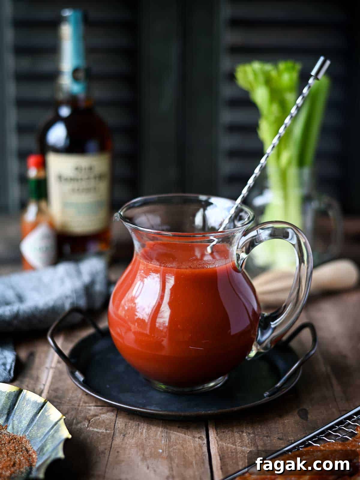 A clear pitcher of bloody mary mix on a wood surface.