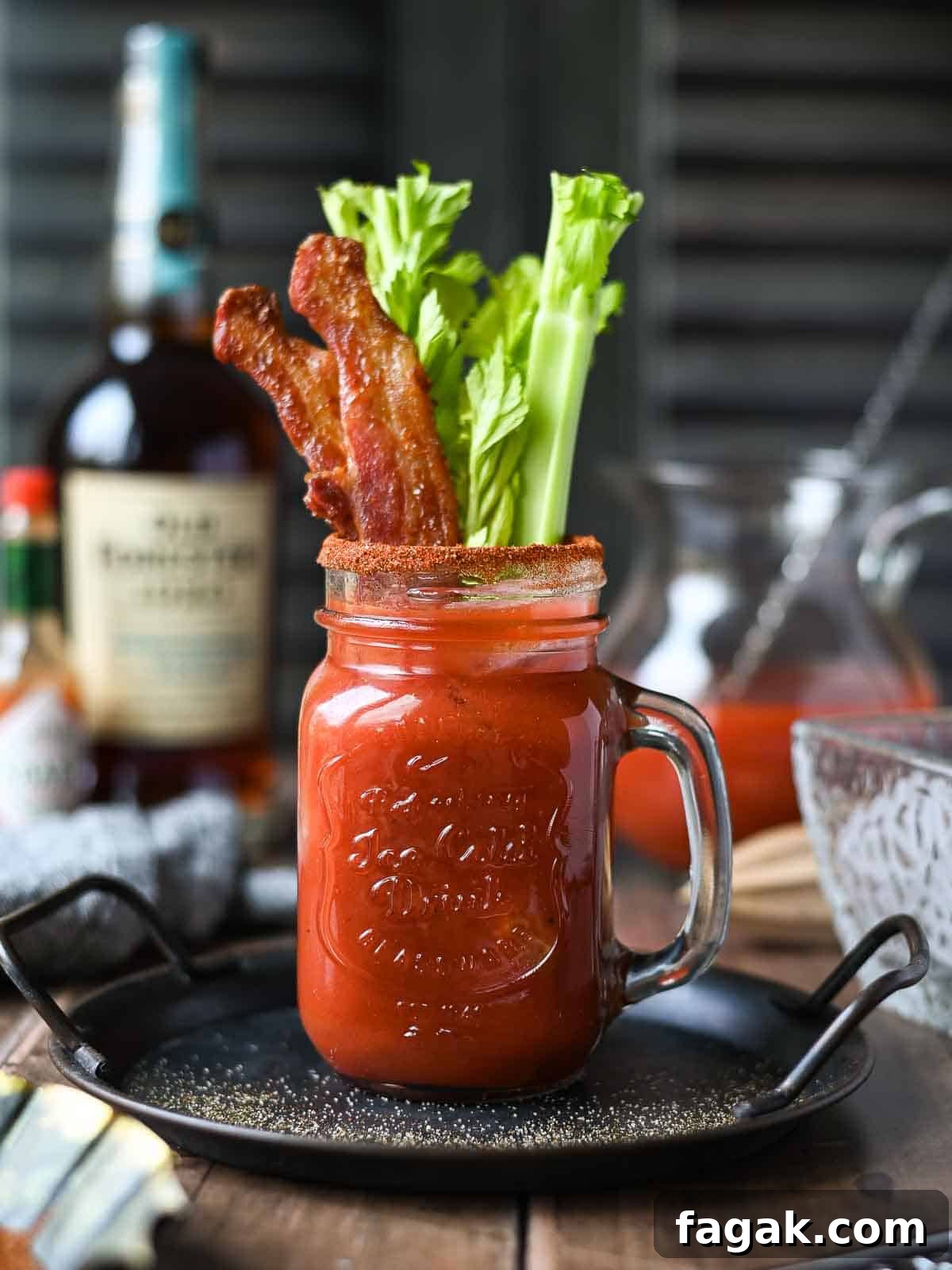 Eye-level view of a bourbon bloody Mary with bacon and celery in a clear Mason jar.
