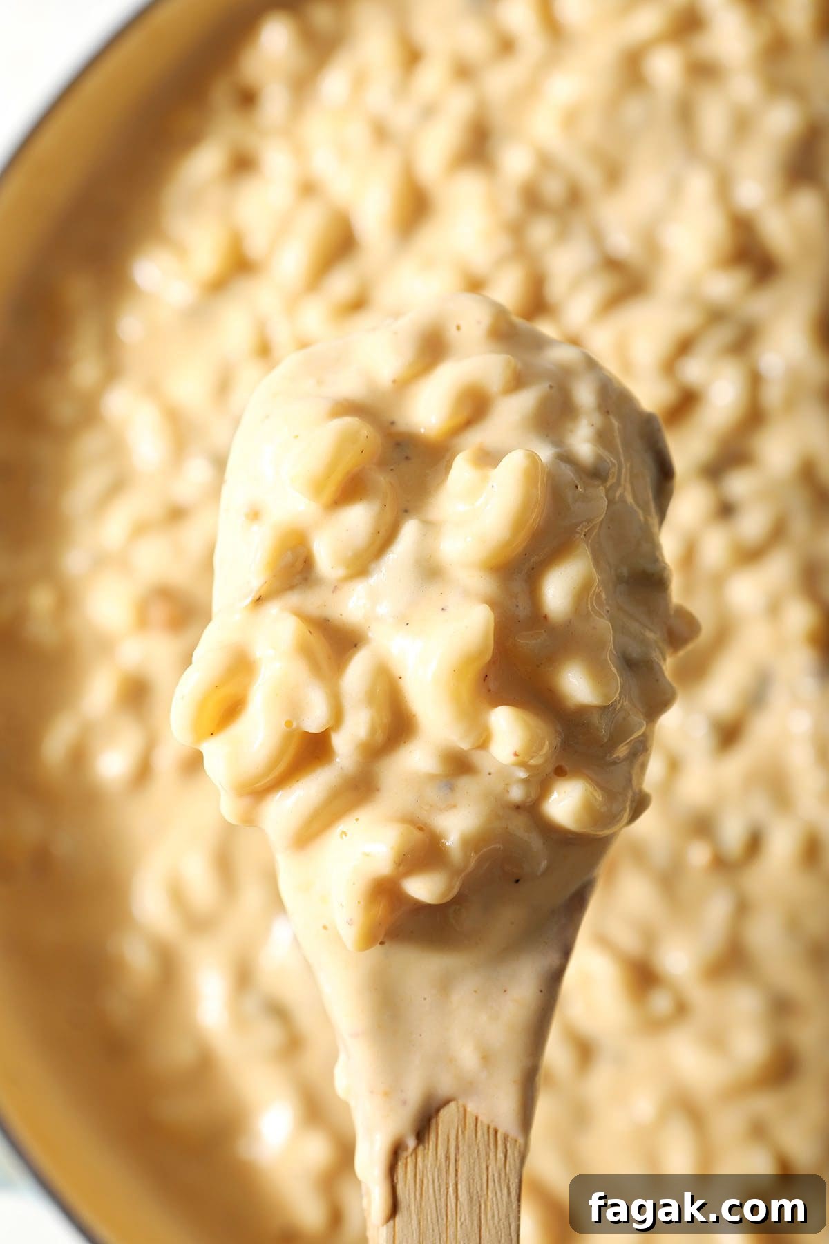 A wooden spoon holds a scoop of macaroni and cheese with green chiles