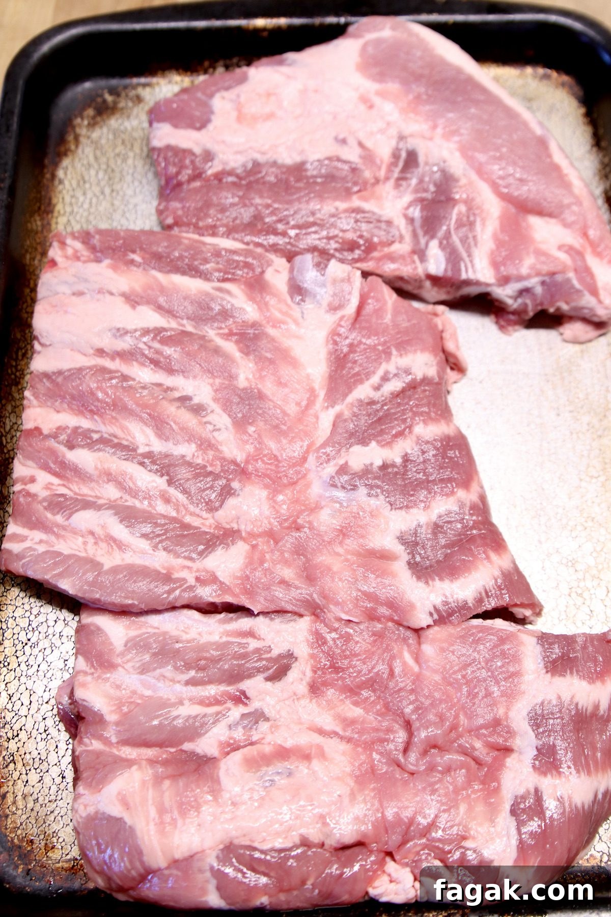 spare ribs - marinade and mop sauce recipe for grilling. rack of spare ribs cut into thirds on a rimmed baking sheet.