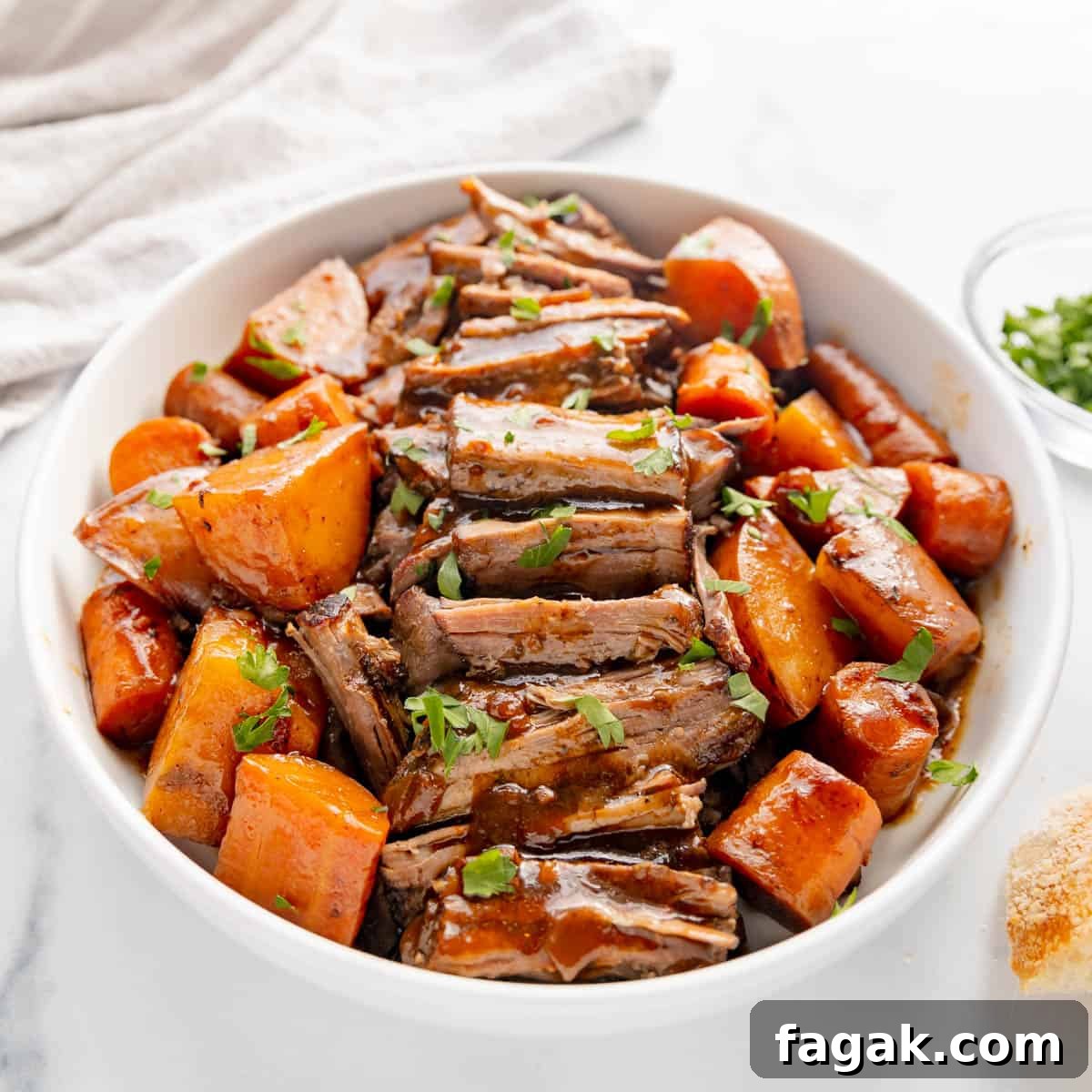 A bowl of sliced pot roast with carrots and potatoes, garnished with herbs on a white surface.