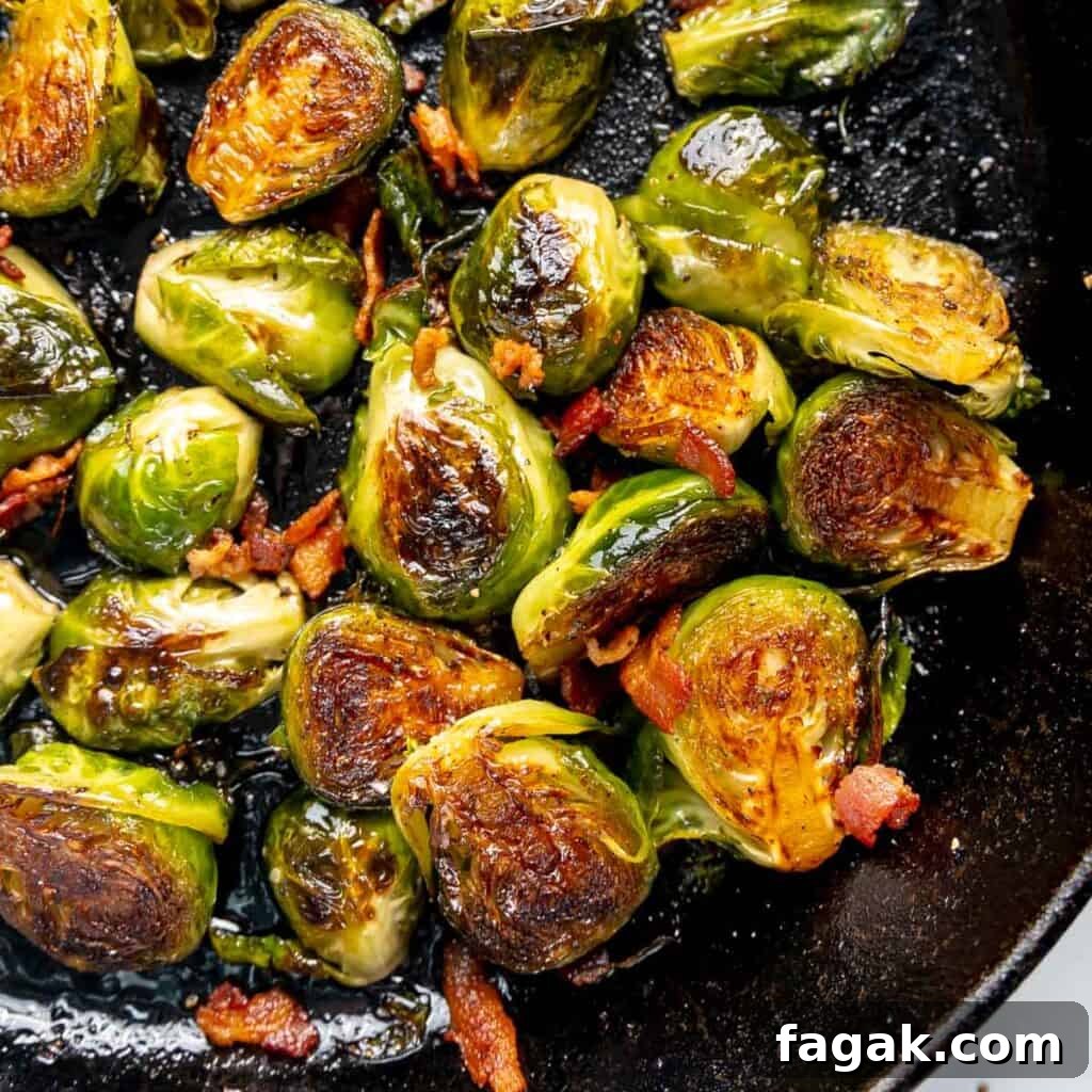 Pan-fried Brussels sprouts with crispy edges and scattered bacon bits in a skillet.