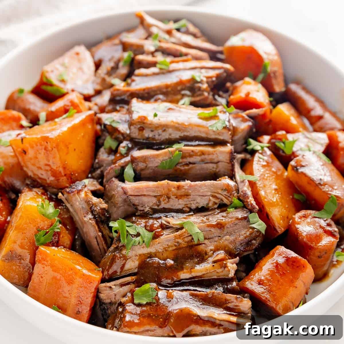 A bowl of sliced roast beef with glazed carrots and potatoes, garnished with chopped herbs.