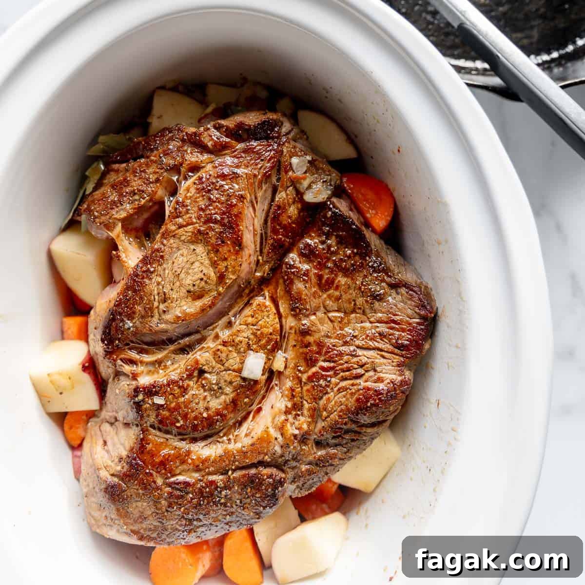 A cooked pot roast with carrots and potatoes in a white dish.
