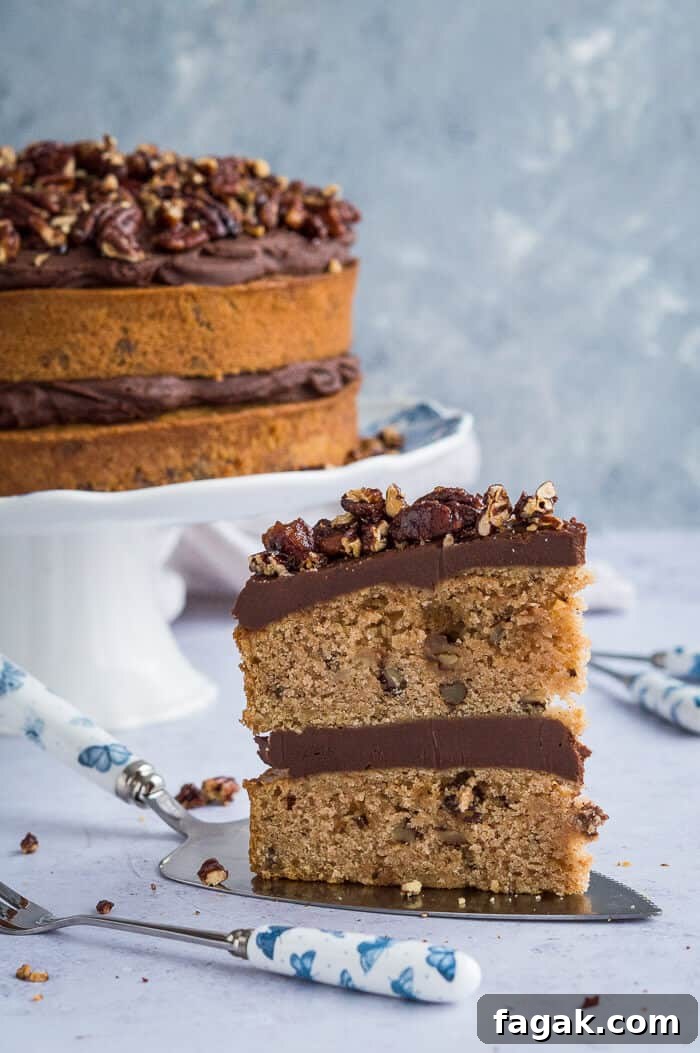 A slice of vegan maple pecan cake with chocolate cashew cream frosting on a cake slice with the rest of the cake in the background.