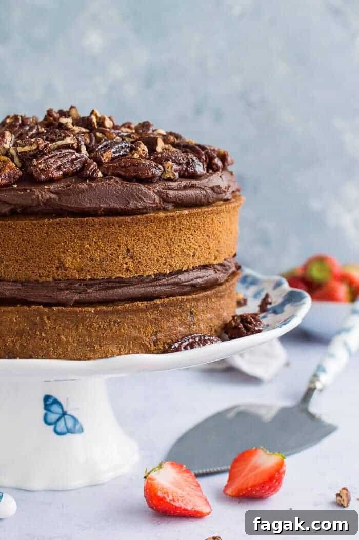 Side shot of vegan maple pecan cake with chocolate cashew cream frosting and maple pecans on a blue and white cake stand.