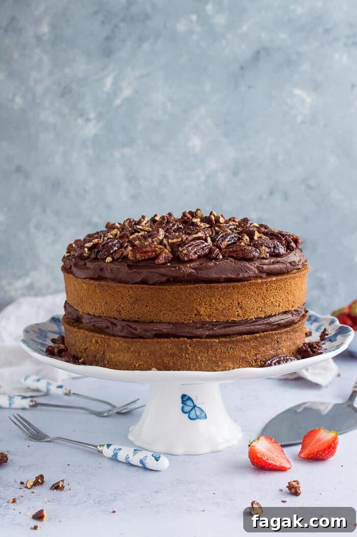 Vegan, naturally sweetened maple pecan cake with chocolate cashew cream frosting on a blue and white cake stand on a grey background.