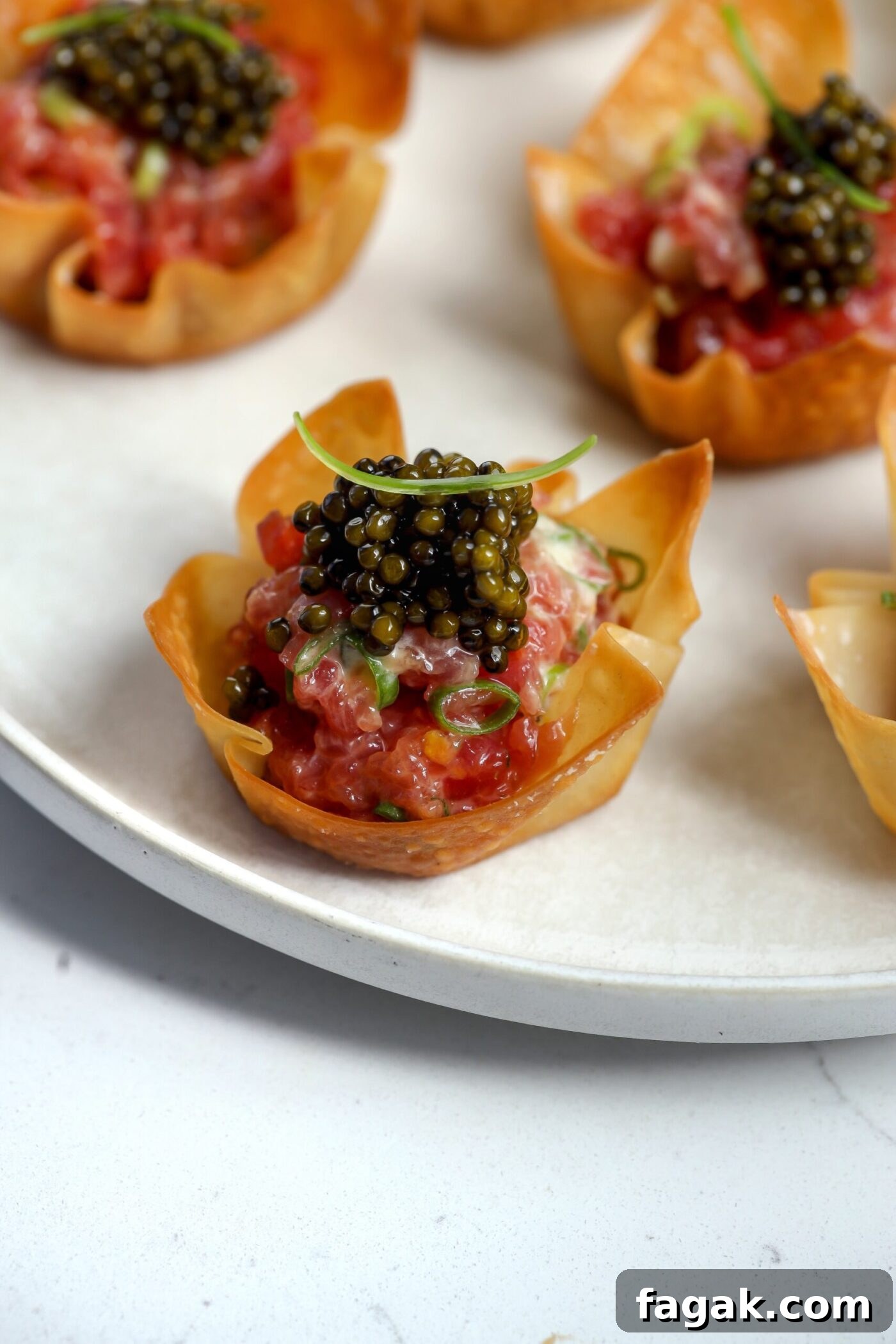 Tuna wonton cups filled with chopped raw tuna, creme fraiche, scallions, and topped with caviar on a serving plate