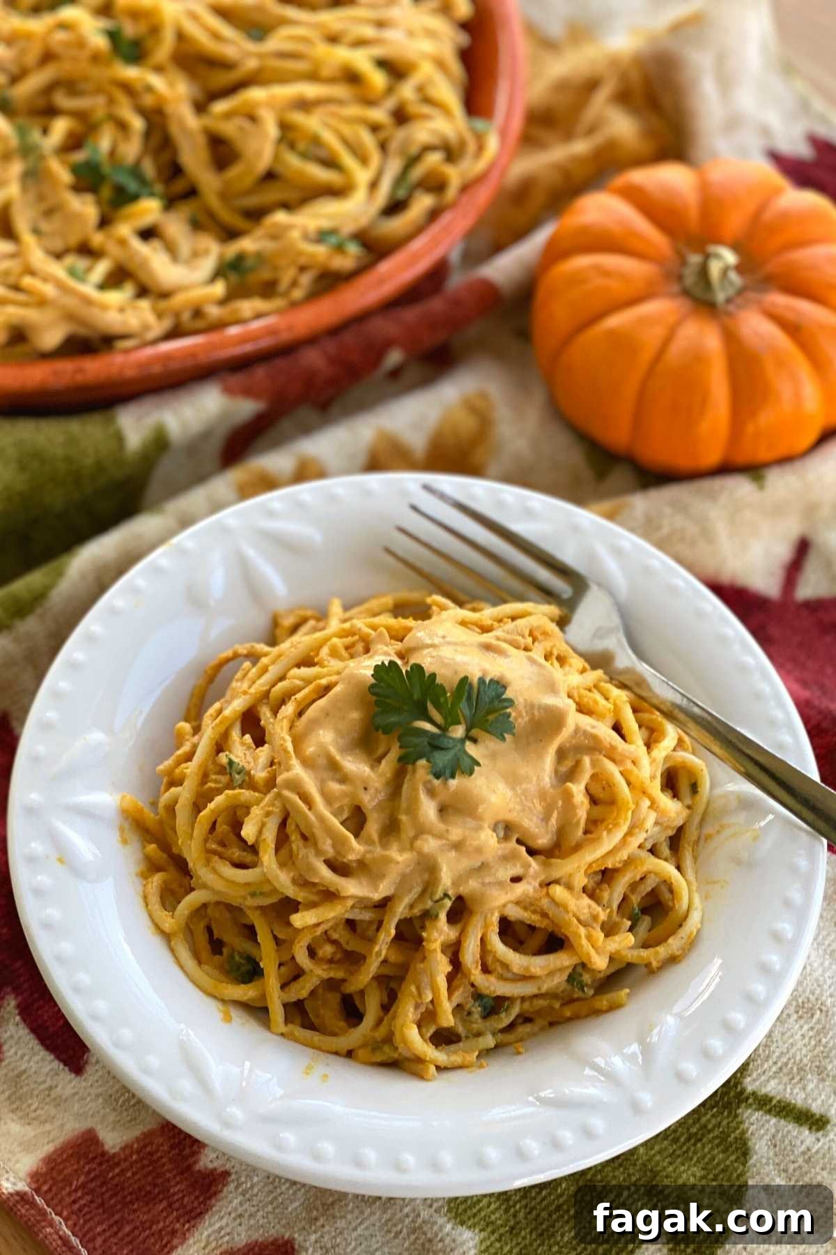 Pumpkin sauce on top of pasta noodles in a bowl with pumpkin and platter behind it.