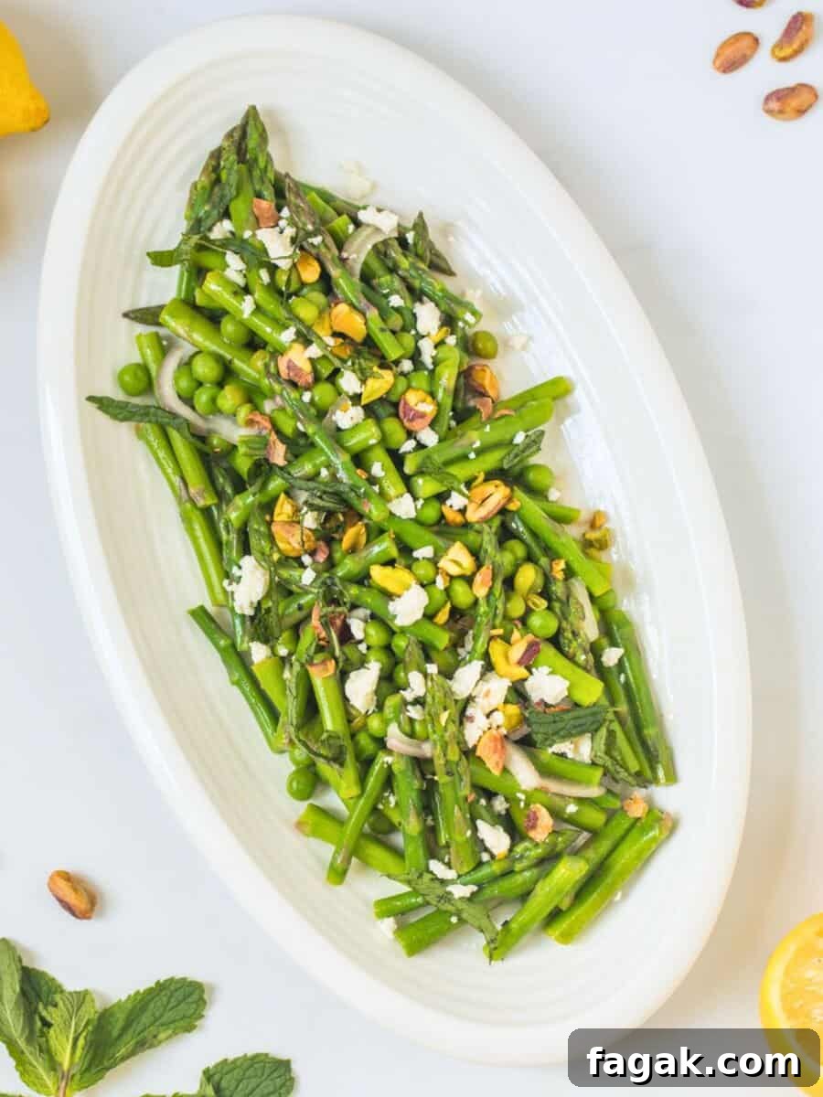 Asparagus salad dressed with lemons served with peas, feta, pistachios, and mint on platter.