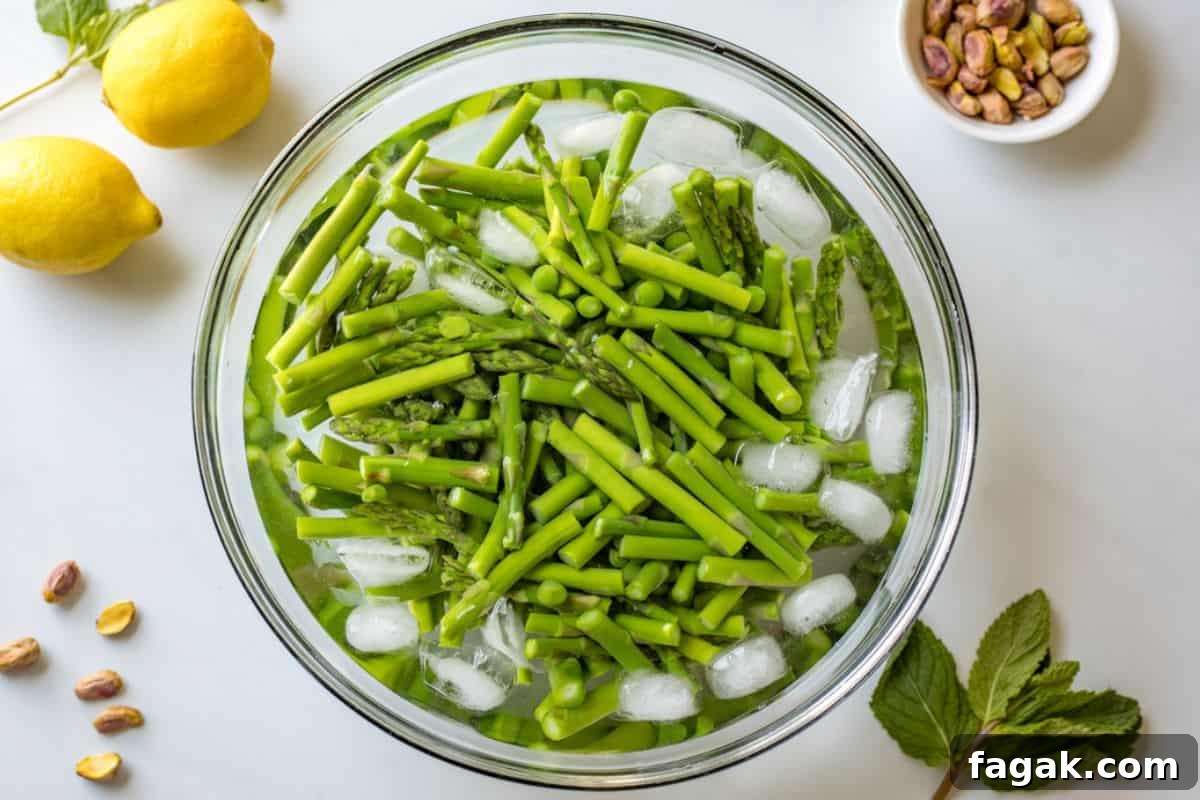 Asparagus and peas in bowl of ice water next to mint and pistachios