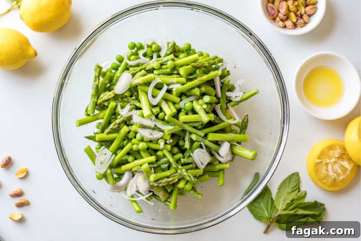 Blanched asparagus and peas in mixing bowl with lemon dressing and thinly sliced shallots.