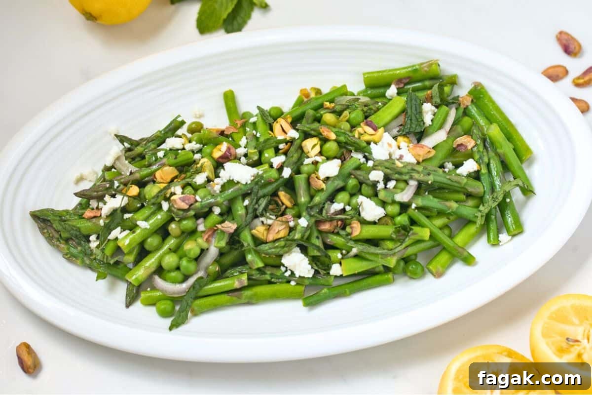 Asparagus and pea salad plated on white plate topped with crumbled feta, chopped pistachios, and mint.
