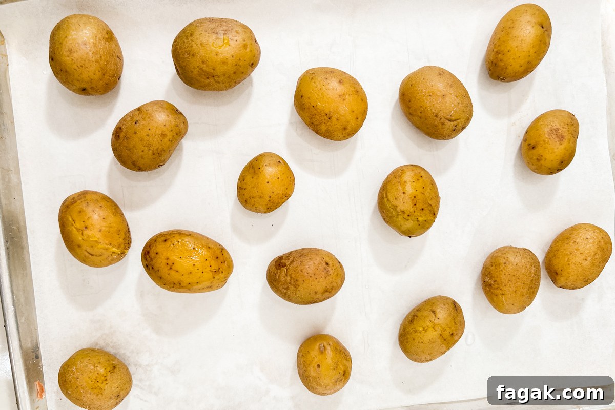 Cooked whole potatoes arranged on a parchment-lined baking sheet.