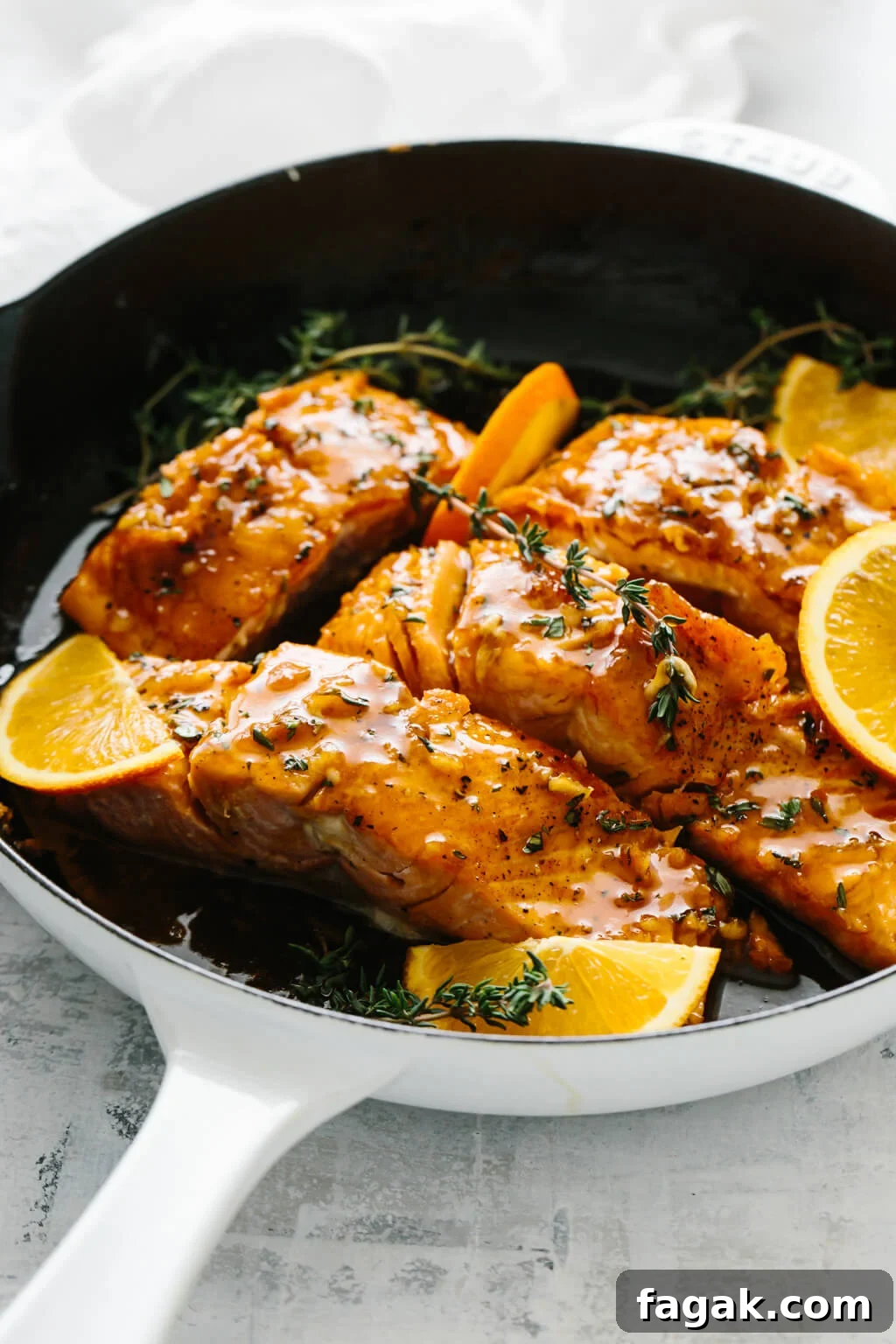 Four salmon filets in a pan with orange slices and thyme on top.