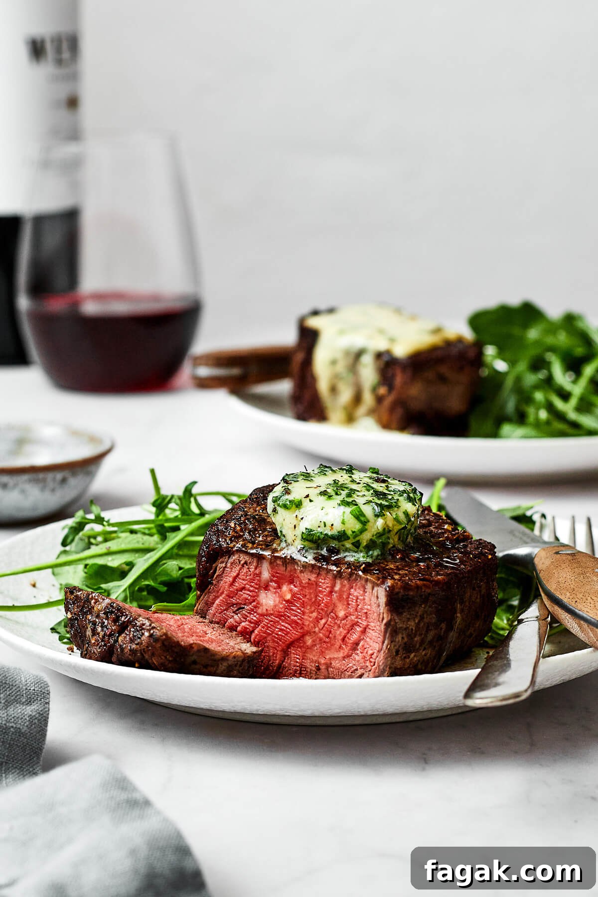 A plate of filet mignon next to a glass of wine