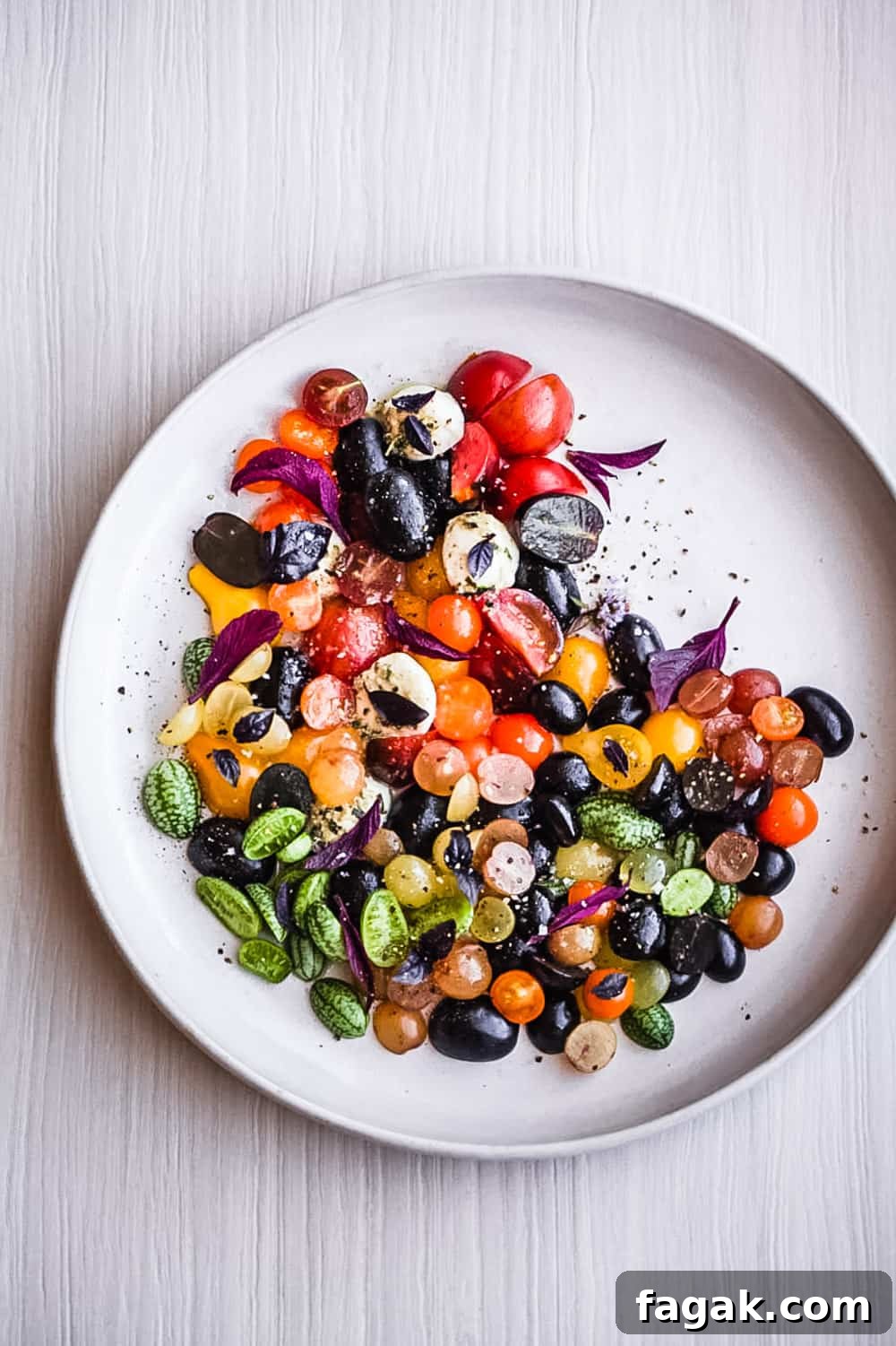 a summer salad with cherry tomatoes, cucuamelons, grapes, basil and cheese arranged on a plate.