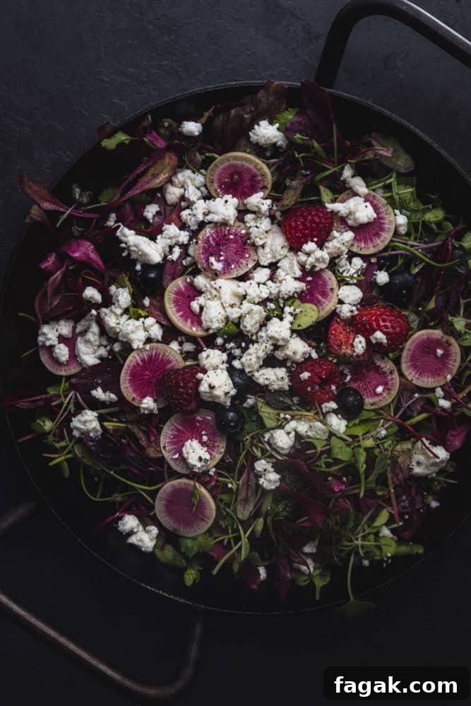 a summer green salad with berries, radishes, and cheese, overhead shot.