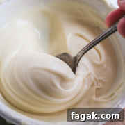close up view of a spoon scooping up thick white chocolate ganache in a white bowl.