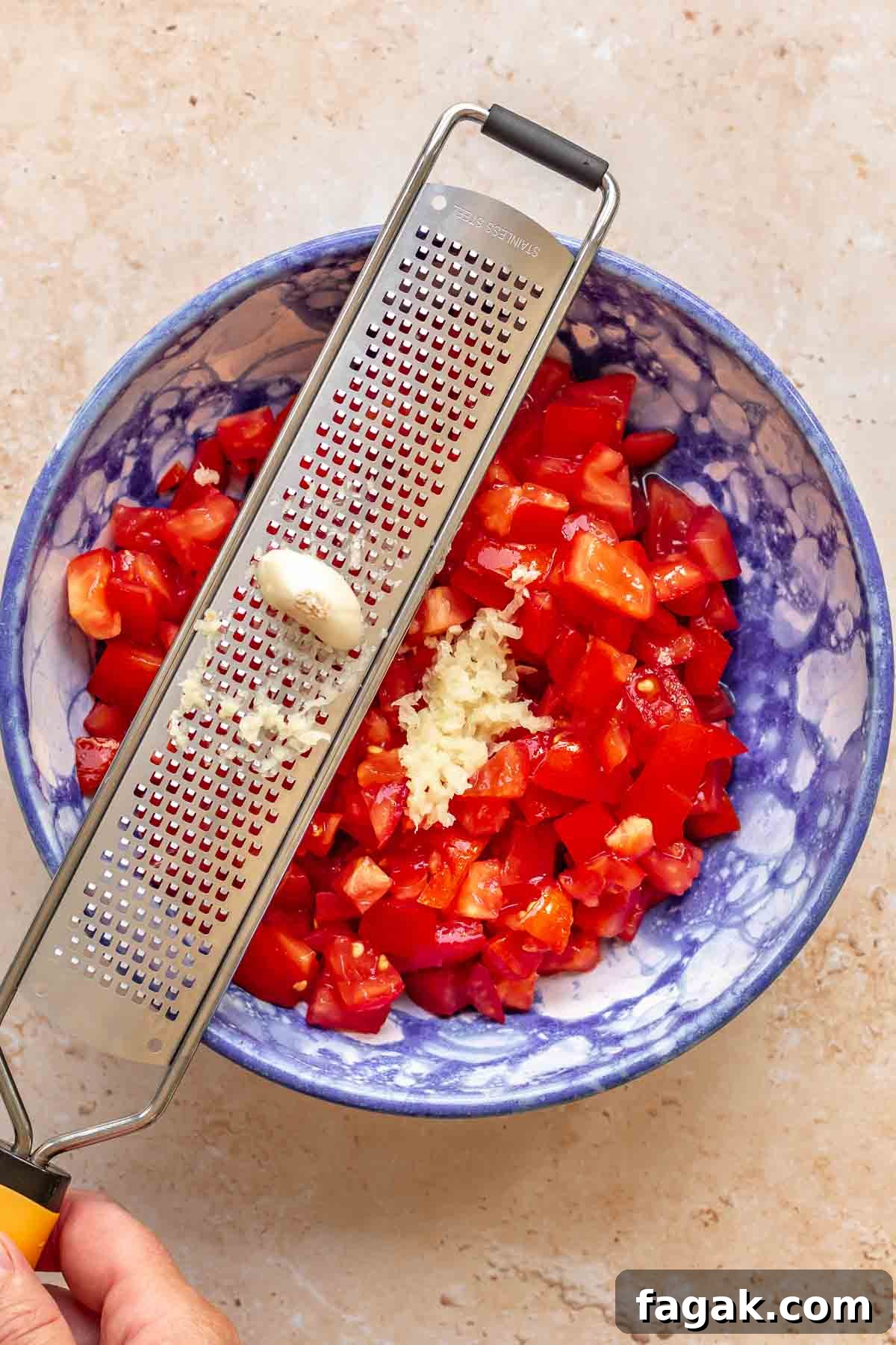 A garlic clove being grated into tomatoes.
