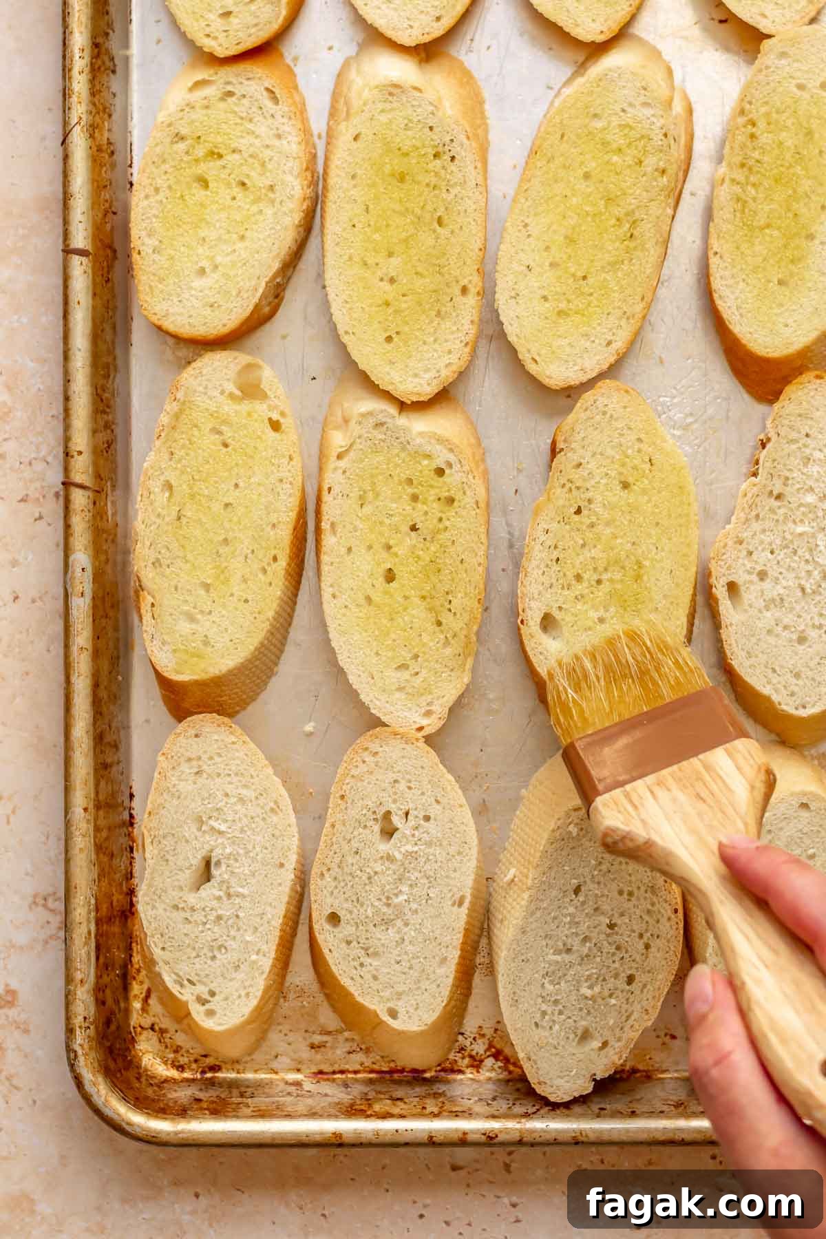 A brush adds olive oil onto bread slices.