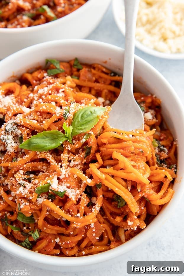 a fork twirling sweet potato spaghetti with tomato sauce in a white pasta bowl