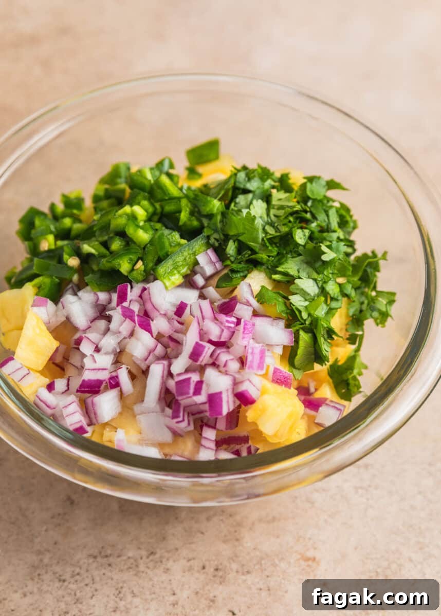 Diced pineapple, jalapeños, onion and cilantro in glass bowl.