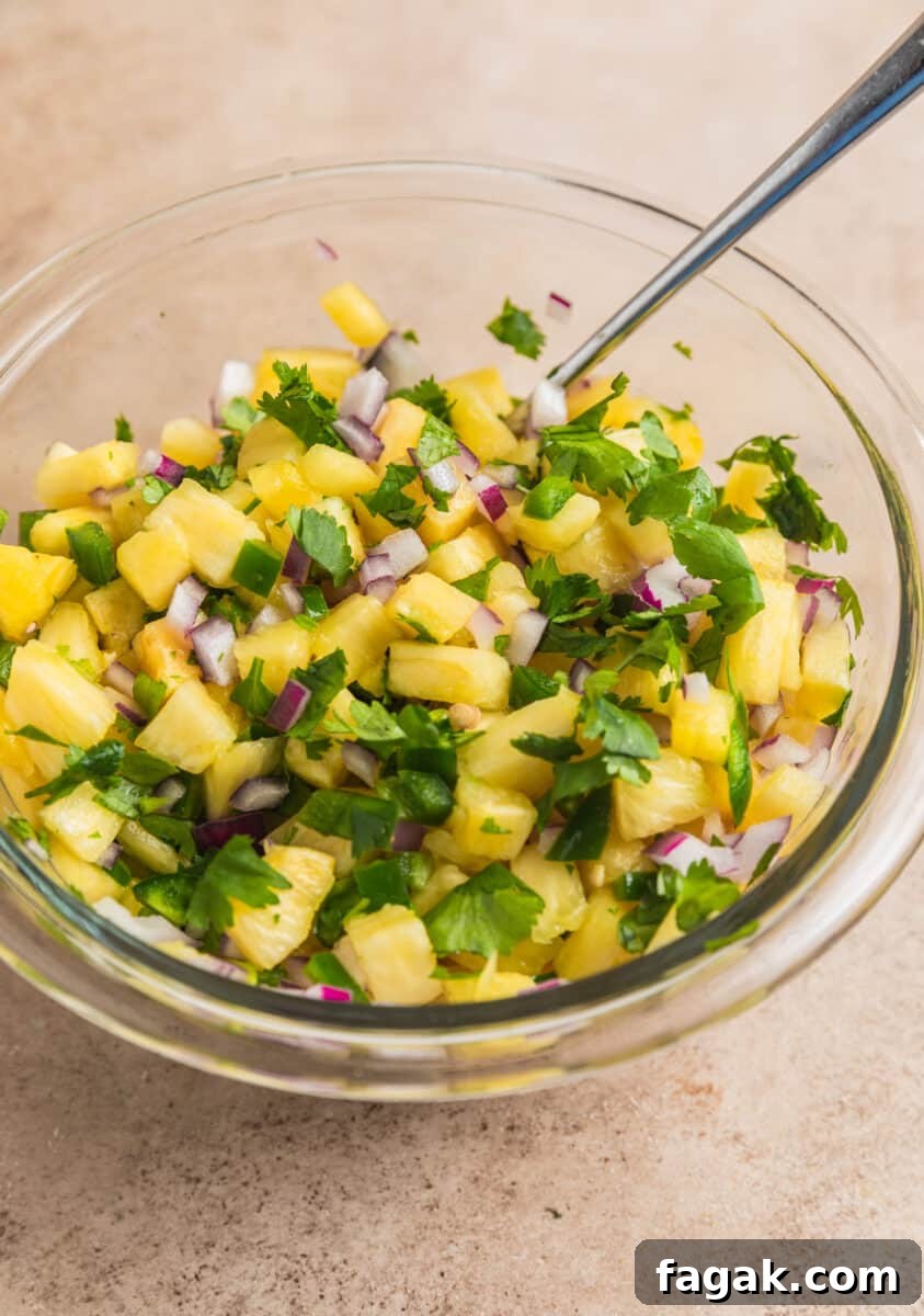 Spoon scooping into glass bowl with pineapple salsa.