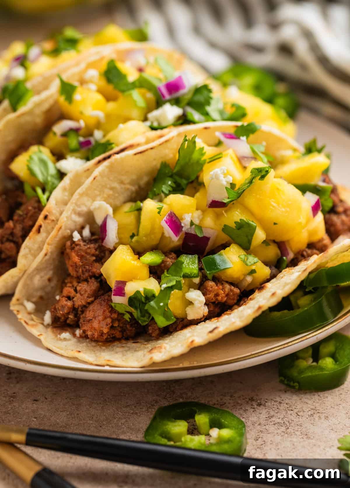 Pork tacos topped with pineapple salsa on plate with sliced jalapeños nearby.