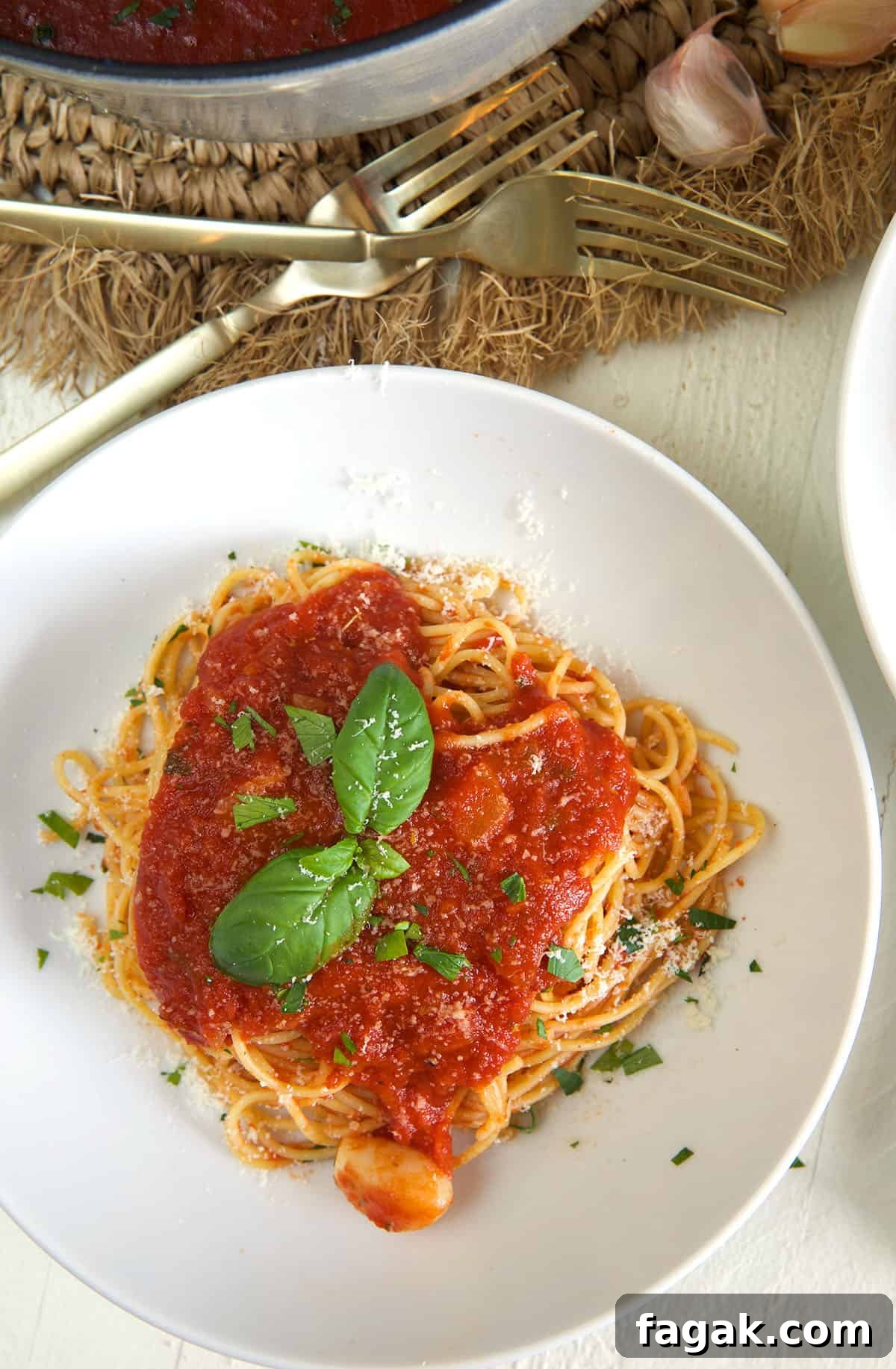 A white plate is topped with a serving of spaghetti and marinara sauce.