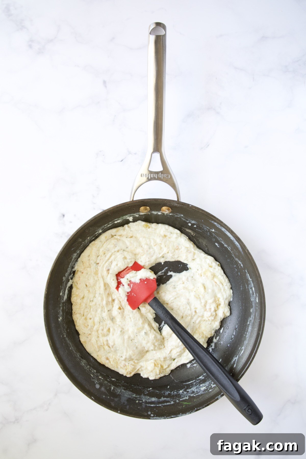 Thickened cheese sauce in nonstick skillet being stirred with red and black spatula.
