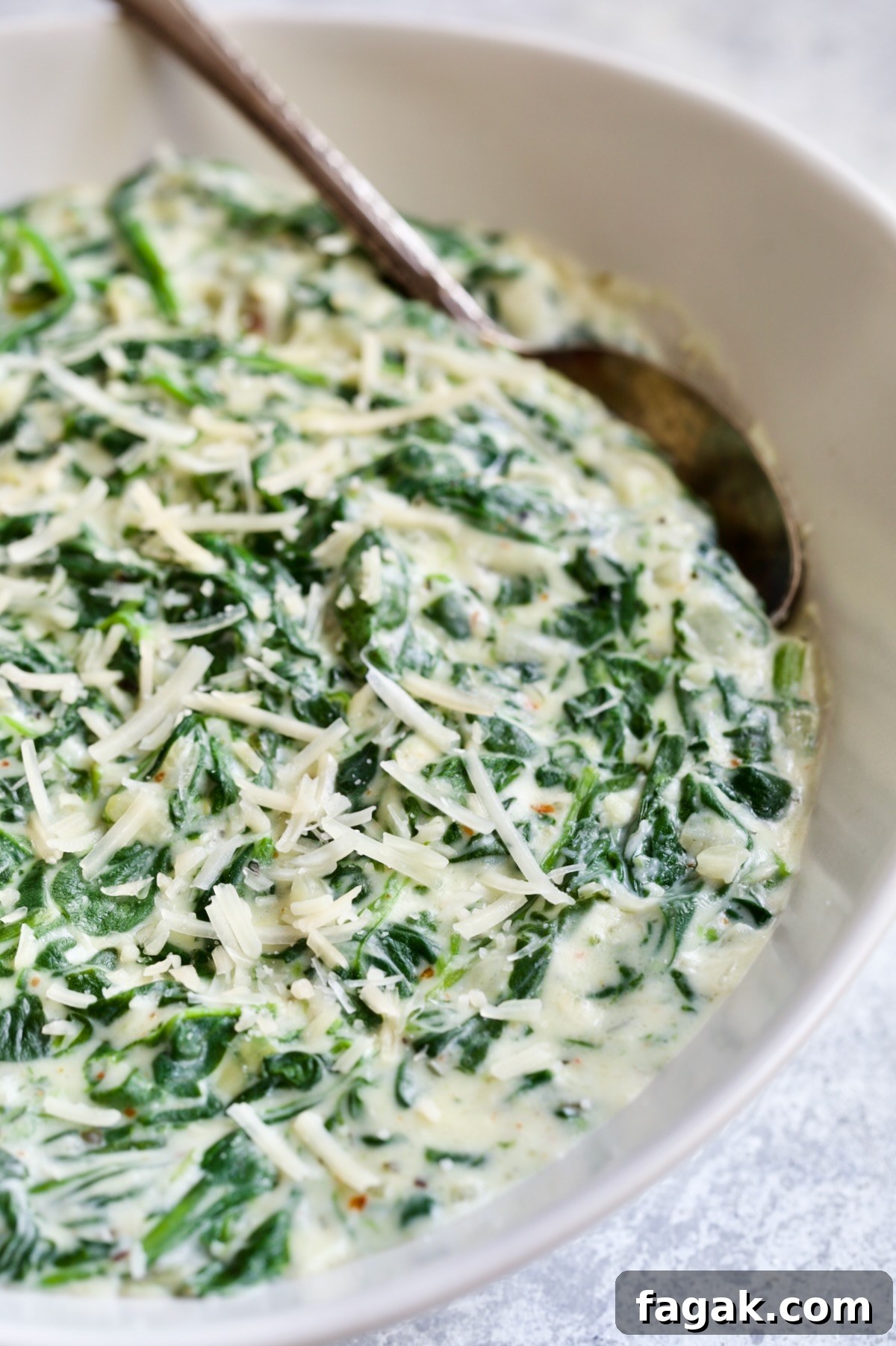 Steakhouse Creamed Spinach in white oval bowl with serving spoon.