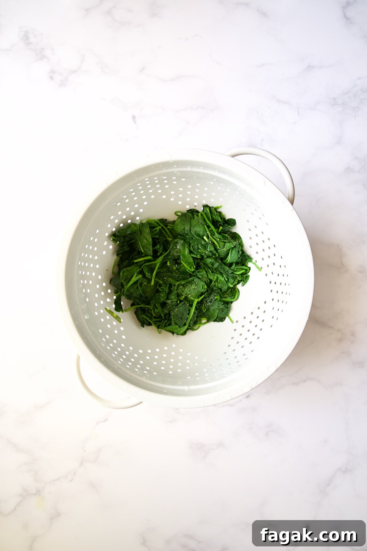 Wilted baby spinach in white colander.