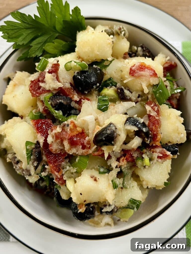 Mediterranean potato salad with parsley garnish in white bowl with black rim on top of a white plate.