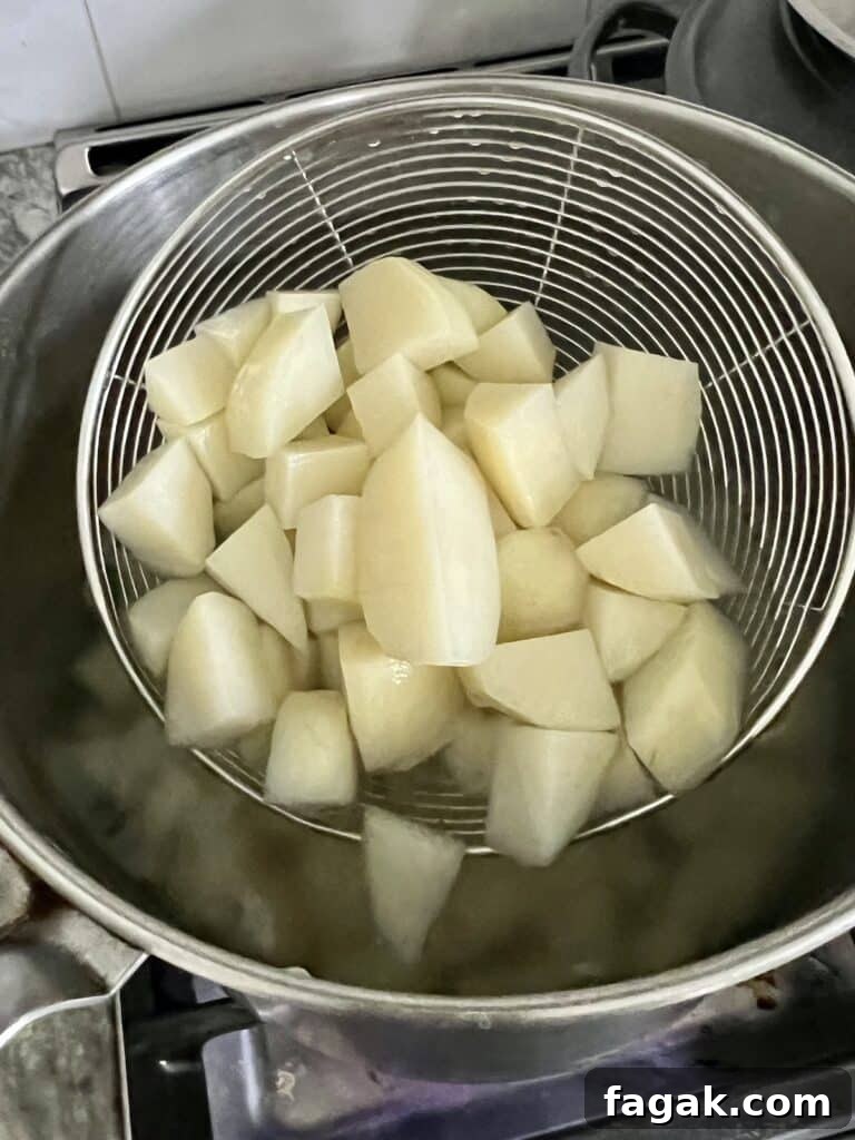 Scooping cooked potatoes out of large pot of boiling water.