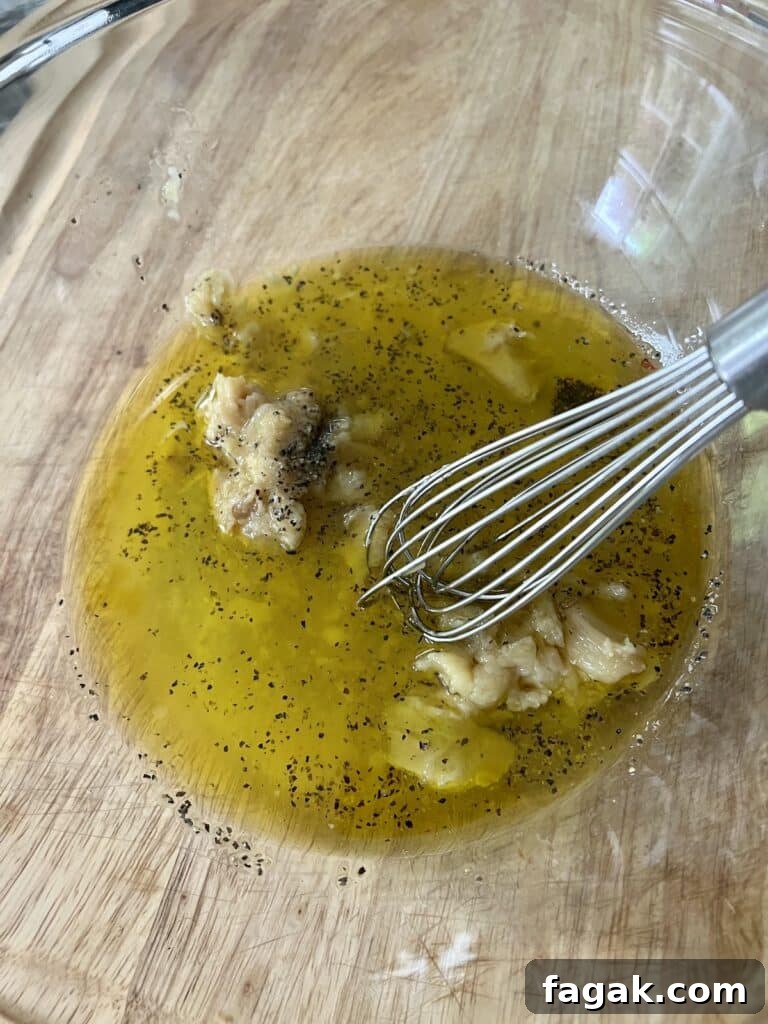 Whisking garlic confit, lemon juice and olive oil together in glass bowl.