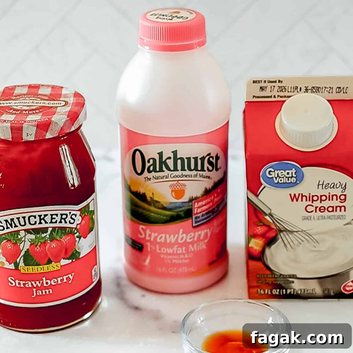 A jar of strawberry jam, a bottle of strawberry low-fat milk, and a carton of heavy whipping cream are placed on a countertop.